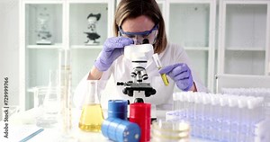 Chemist holds test tube with oil and looks through microscope in research laboratory. Testing concept of oil properties