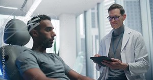 Futuristic Laboratory: Male Patient Wearing Headset for an Advanced Brain Scan, Monitored by a Doctor Using Digital Tablet Computer. Neural Disease Research and Cognitive Optimization Using Technology