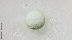 Bath bomb ball dissolves in water with white foam bubbles. Cosmetic product and skin care. Clear water with reflections, refraction sunlight and shadows. High quality 4k footage. High quality 4k