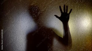 shadow of human figure on a glass screen, holding hand and moving back, silhouette of alien