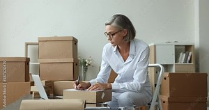 Attractive mature businesswoman, small business owner prepare goods for sending, writes customer data, shipping parcel box using fast and safe transporting services. Shipment, delivery, dropshipping Stock Video