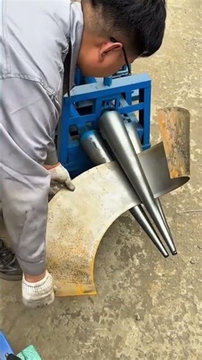 Worker shaping curved metal sheet using blue cone roller bending machine on workshop floor