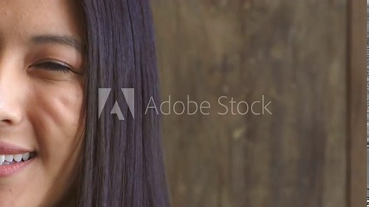 Shy teenage girl feeling self conscious and insecure. Face of a female with social anxiety giving a timid giggle and nervous laughter. Close up of pretty Asian woman smiling at the camera