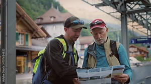 Two travellers reading paper map on railway station on tour in Switzerland