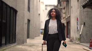 Download A black woman is getting ready for work in an office uniform in a public downtown area, carrying all her work equipment including a computer and a phone. for free