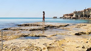 Young girl looking stand on rocky formations by sea cave in Ayia Napa, Cyprus. A shot from the inside of a sea cave in sunny Mediterranean coast of greek Cyprus.Grotto sea cave