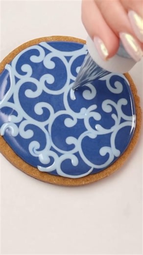 SweetAmbs - Amber Spiegel on Instagram: "This wet on wet royal icing cookie is a simplified version of my filigree design. I love this simpler version because it’s easy to do and looks so pretty! I combined two shades of blue icing with a red bead border for this Christmas cookie color palette. The tutorial and recipes are in the Cookie Art Club! #howto #christmascookies"