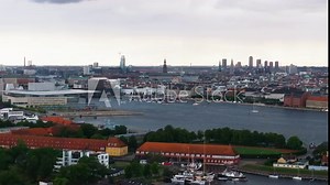 Copenhagen's cityscape showcases a blend of modern architecture, historic buildings, and green areas under a cloudy sky, with water and harbor views enhancing the urban landscape
