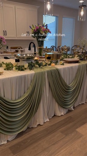 Kitchen island setups just got a massive upgrade! ✨ Look at how Flavor House By Jia layered these heavy sage swags to create the ultimate buffet backdrop. The depth of those fabric folds is everything! 💕 Tag @thetableclothsfactory in your next setup so we can see how you style your space! - - - #buffetstyling #drapingdesigns #eventdecor #kitchenisland #partyplanning #cateringideas #draping #buffet