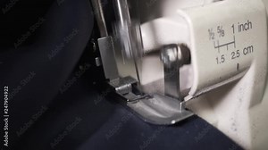 Seamstress sews clothes made of blue cloth on a sewing machine. Work by the light of the built-in hardware lamp. Steel needle with looper and presser foot close-up