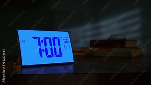 Digital alarm clock waking up at 7 AM. Close-up view. The numbers on the clock screen changes from 6:59 no 7:00 AM. Then alarm logo appears on the screen.