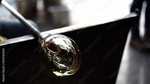 A glass blower rolling a piece of molten glass to shape it into art