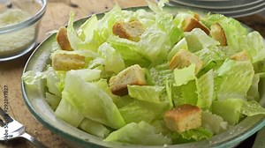 A delicious caesar salad with croutons and creamy dressing on a rustic table top.