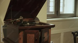 Old mechanical wooden phonograph for playing vynil gramophone records in the interior of a mansion. Portable version of the gramophone with a spring engine and a large tonearm, close-up.