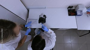 Two scientific lab assistant saw in laboratory microscope scientific discovery, they are happy to laugh and clap their hands writing data in document. Dressed in a medical white work uniform. Top view