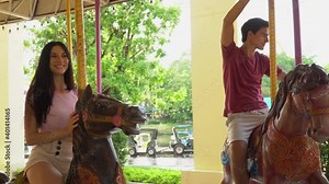 couple in love riding on carousel together at the amusement park outdoors in summer having fun in vacation
