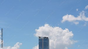 Time-lapse clouds moving above tall commercial building skyscraper real estate