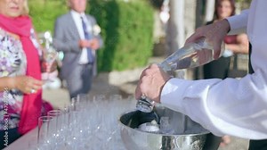 Formal party celebration in the open air, elegant guests on banquet party, waiter serving people at the banquet table. Servant pouring water into glass for invited middle-aged woman. Pouring beverages