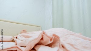 A young girl with a sleep mask wakes up in the morning in a bed with pink bed linen