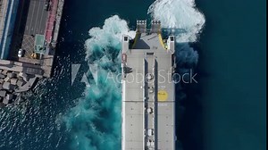 Top down aerial view fast ferry docking at port for loading and unloading. Modern high speed passenger ferry ship reaching destination. Engines pushing water against pier with white foam in blue water