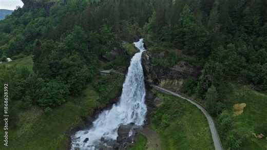 Steinsdalsfossen waterfall near Norheimsund in Vestland, Norway. Tall cascade plunging through forested cliffs with a walking path behind the water during lush summer conditions.
