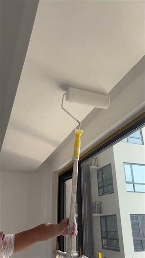 Interior ceiling painting with roller near window during renovation