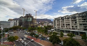 An elevated Time Lapse view of a busy intersection in Cape Town CBD, South Africa with construction in the foreground and Table Mountain in the background. Moving cloud over a blue sky.