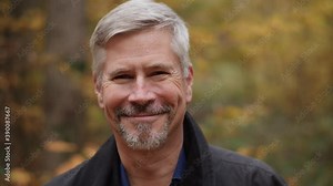 Portrait of a smiling handsome middle aged man in nature, slow motion. Mature caucasian man laughs and shows real emotions being happy, joyful and confident. Attractive autumn forest background.