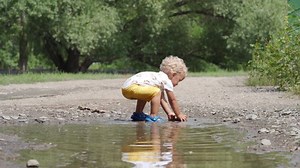 Happy child having fun playing in a puddle of rainwater in summer park. 1.5 year old toddler kid on the nature outdoors.