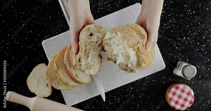 Breaking bread on the cutting bord. Fresh baked bread, sliced bread on background. Preparing food at black table.