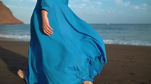 Legs of a woman in beautiful blue dress walking along a black volcanic beach