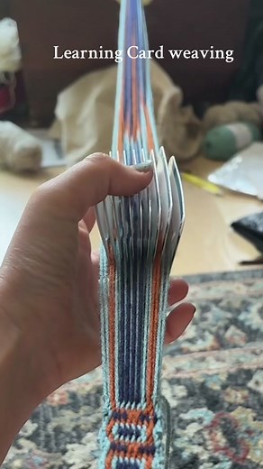 Relaxing while learning card weaving. Im still not understanding how the cards rotation makes l which color show, but its working if I follow the directions. Using the left over yarn from the #chestnutcardigan. Set up is a set of cards, a bobbin, and a book(card weaving by candice crockett). #cardweaving #knittok #schacht