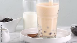 Stirring tapioca pearl bubble milk tea in drinking glass, tasty taiwanese popular drink on bright marble table. Homemade concept. 4K shot video.