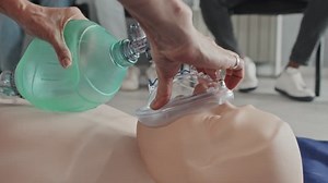 Close-up of unrecognizable paramedic performing CPR on dummy with use of bag valve mask for artificial ventilation and doing heart massage