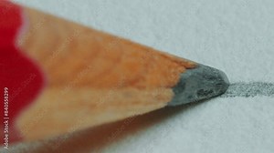 Tip of graphite wood pencil moving slowly and drawing a line on paper. Extreme close-up view