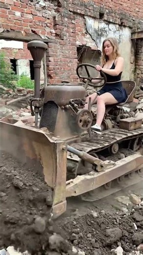 A woman is driving a bulldozer to push a pile of dirt