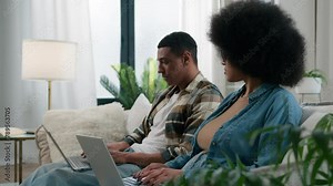 Gadget video game addict family computers addicted African American couple on couch at home ignoring using two laptops sad African American woman wife girlfriend looking on husband man exhale stress