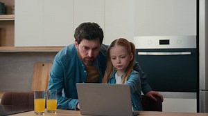 Happy family little daughter child kid girl using pc e-learning home distant education studying remote play game in kitchen adult father care dad help with laptop using teach browsing computer control