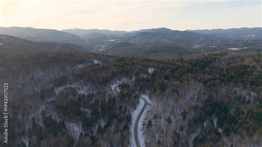 4K winter drone video of the snowy green mountains of Vermont with a rural country road covered in snow in the distance. New England, USA.