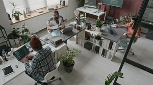 Wide top view of three multinational male and female software developers working together in office at IT startup - writing computer code, discussing algorithm idea while developing mobile application