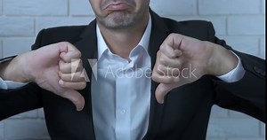 Negative thumb sign. A man negatively show his thumb dowm in the office.