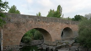 Set against the scenic backdrop of Avila, Spain, the medieval Roman bridge crosses the Adaja River, featuring impressive granite arches and a storied history from the 1st century.
