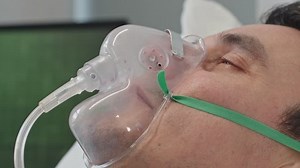 Closeup of man breathing through oxygen mask while lying on hospital bed
