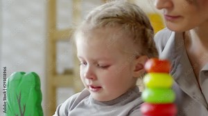 Close-up shot of upset little girl crying while playing in kindergarten. Careful female teacher wiping her tears and trying to calm down