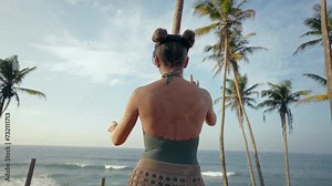 Woman in VR headset explores tropical beach, interacts with augmented reality game, gesturing, immersive tech experience in nature, feels ocean breeze, virtual travel in sunny exotic locale.