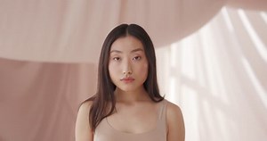 Young cute asian girl model washing off light nude makeup with cotton pad smiling posing. Close-up portrait beautiful woman with light beige background. Natural beauty concept.