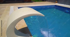 Artificial waterfall. Clear transparent water falls on the background of blue water and marble. pool in the hotel. slow motion footage.