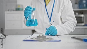 Scientist in lab coat analyzes blue liquid in a flask at a laboratory workbench with paperwork and pen Stock Video