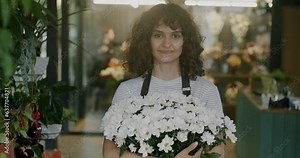Portrait of cheerful saleswoman in uniform standing in flower shop holding beautiful bouquet and looking at camera. People and gift store concept.