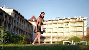 A woman with dumbbells works out on the street, training her legs and buttocks, sunlight and clear sky create ideal conditions for effective outdoor training.